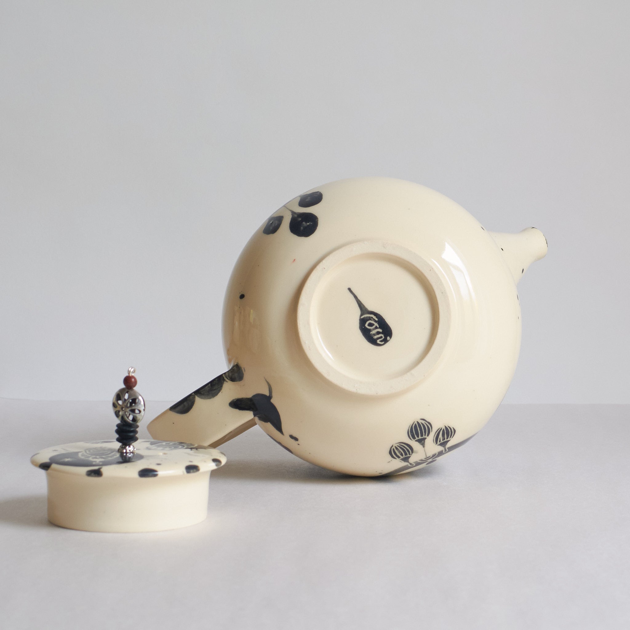 Black and white earthenware teapot with beaded pull on a white background