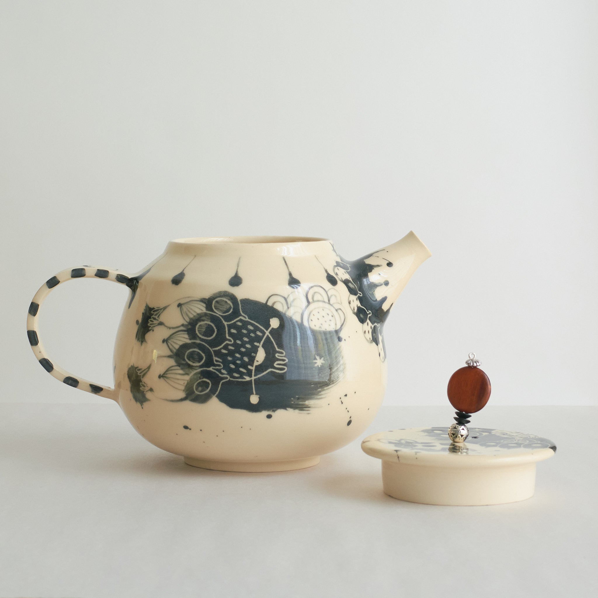 Black and white earthenware teapot with beaded pull on a white background