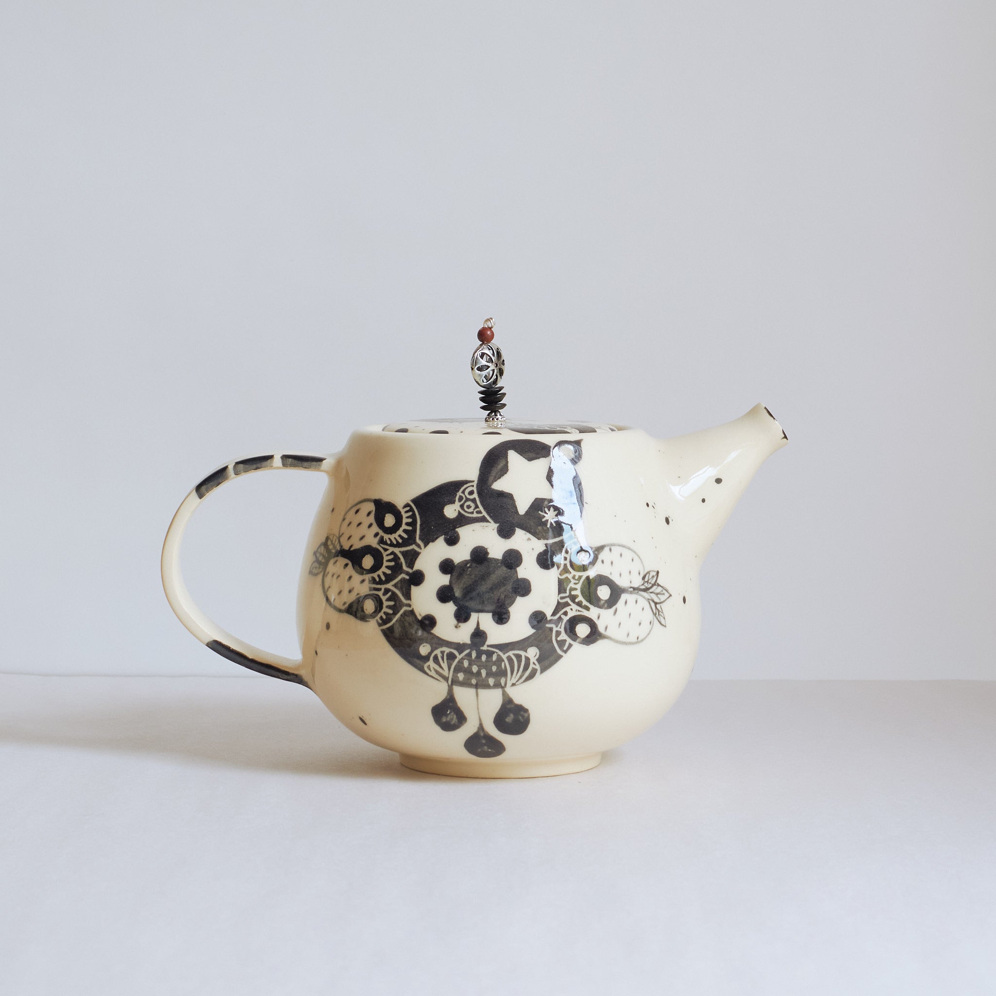 Black and white earthenware teapot with beaded pull on a white background