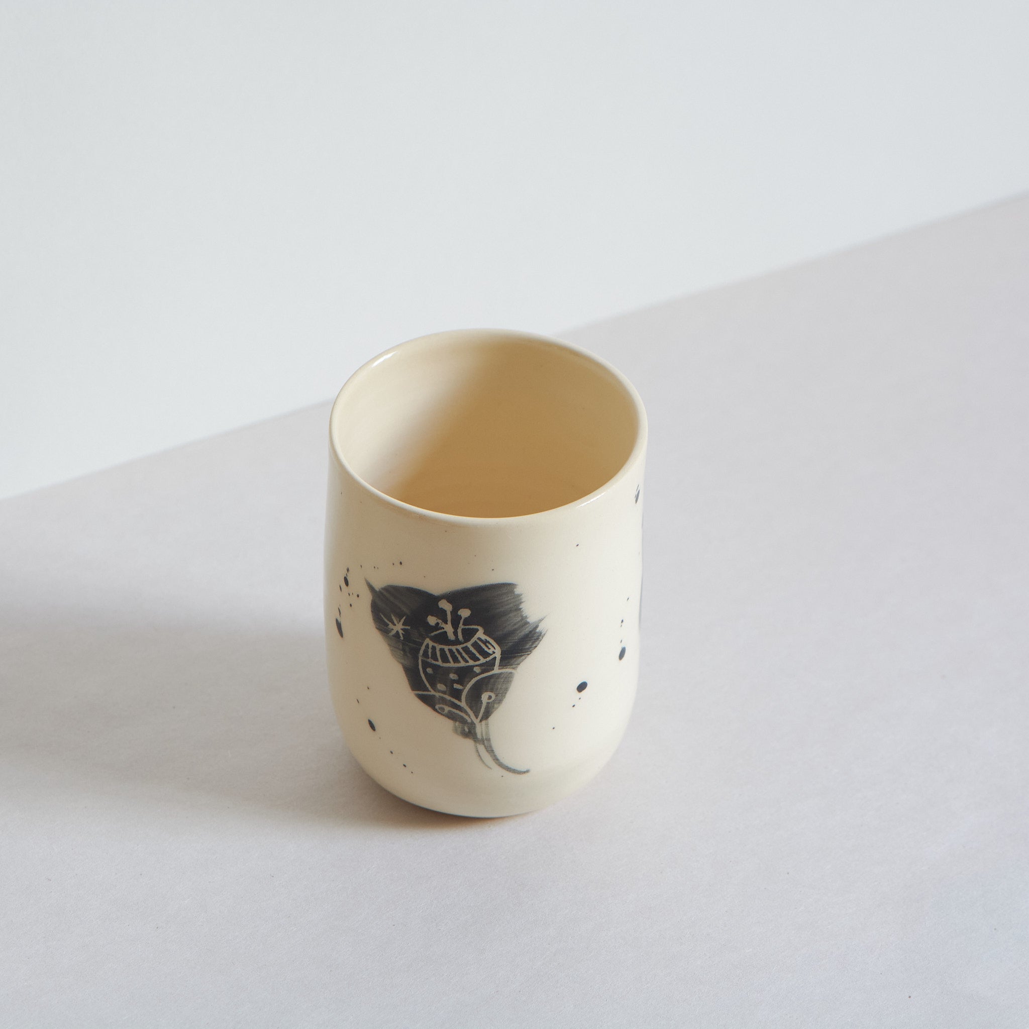 Side view of black and white earthenware tumbler with carved patterns on a light background
