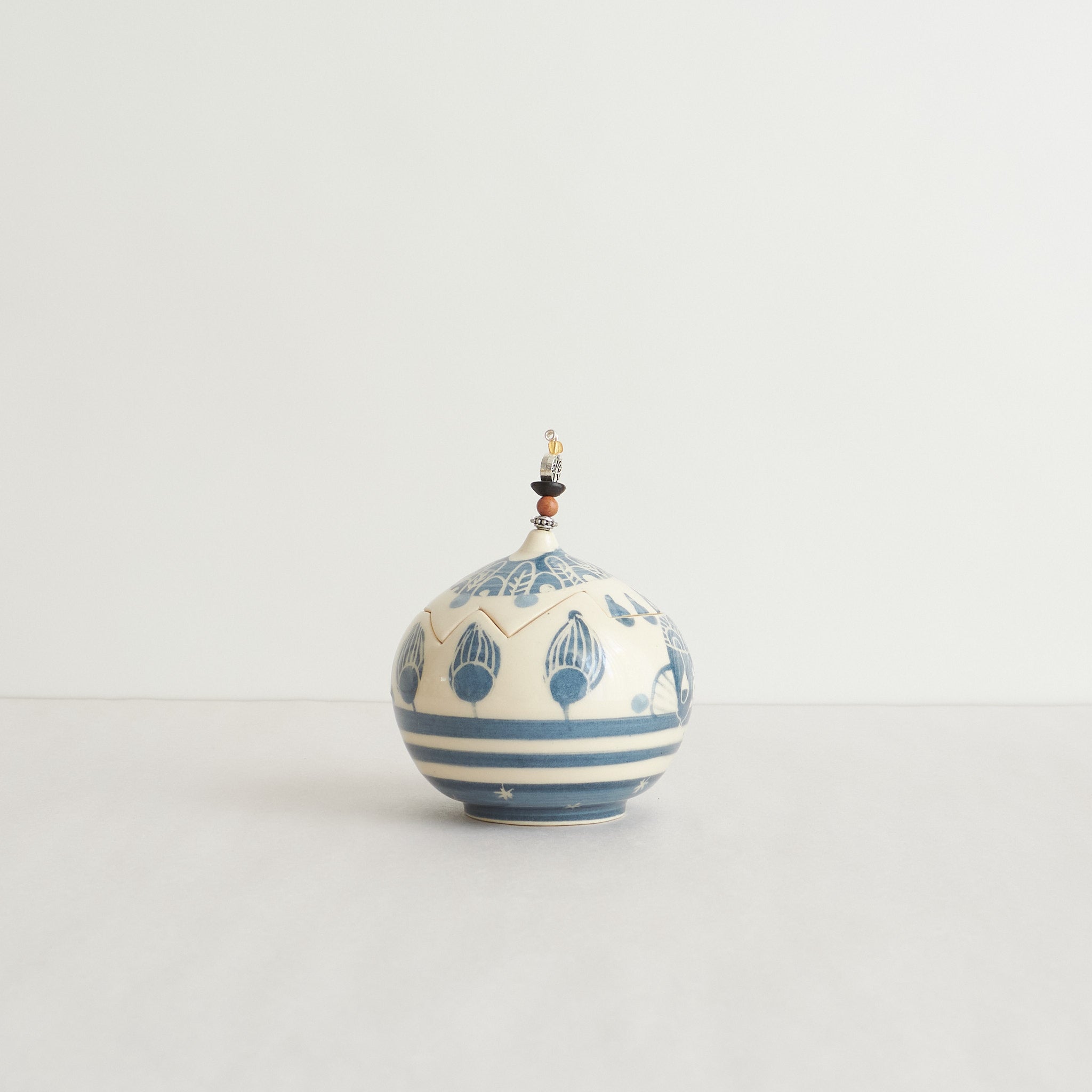 Earthenware lidded box with blue carvings and beaded pull on a light gray background