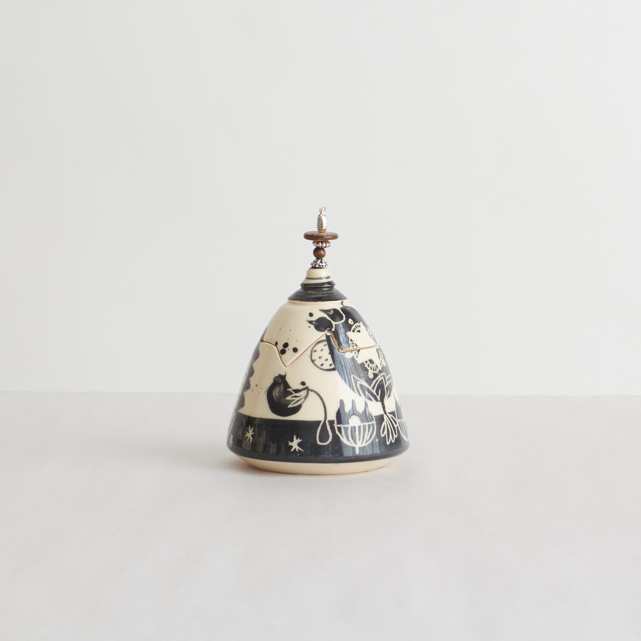 Earthenware lidded box with black carvings and beaded pull on a light gray background