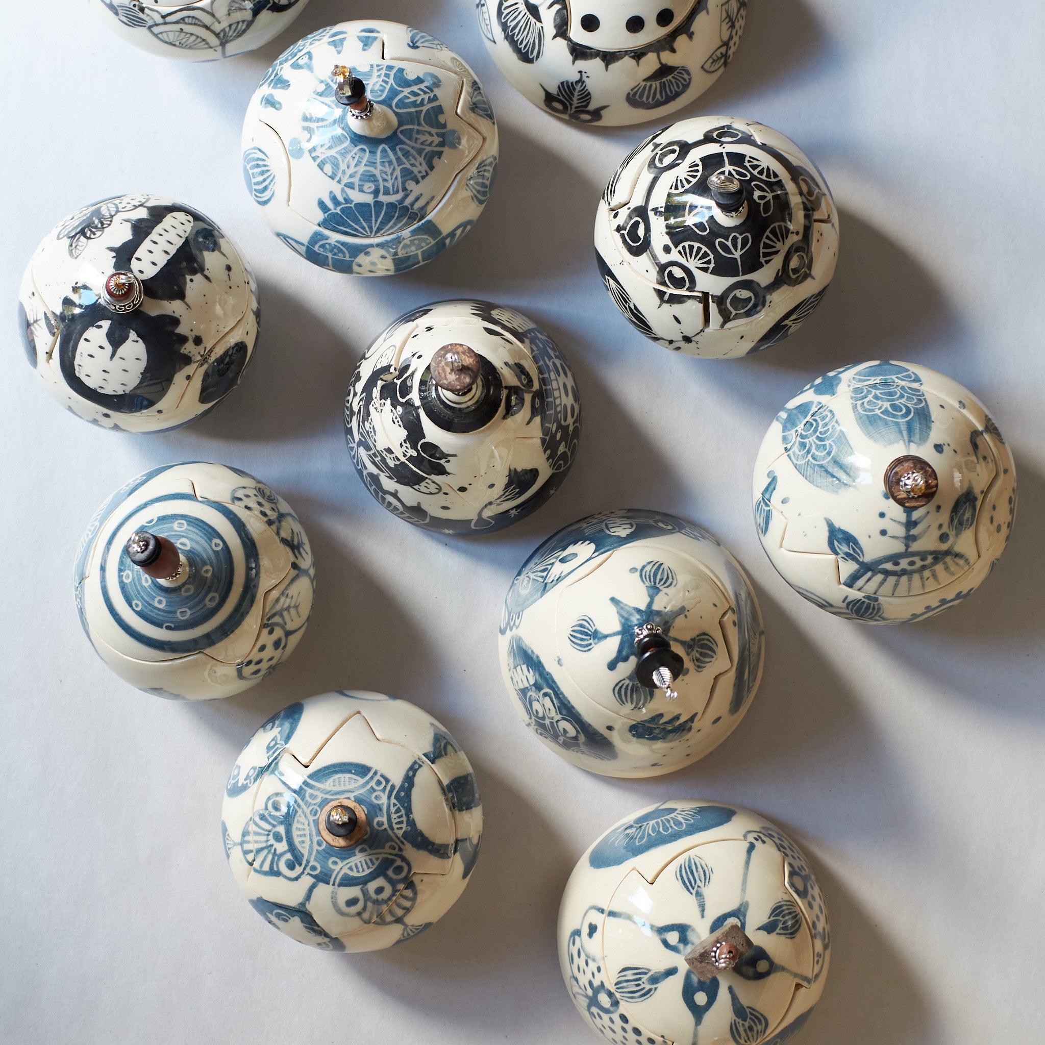 Top view of decorative earthenware lidded boxes with blue carvings and beaded pulls on a light gray background