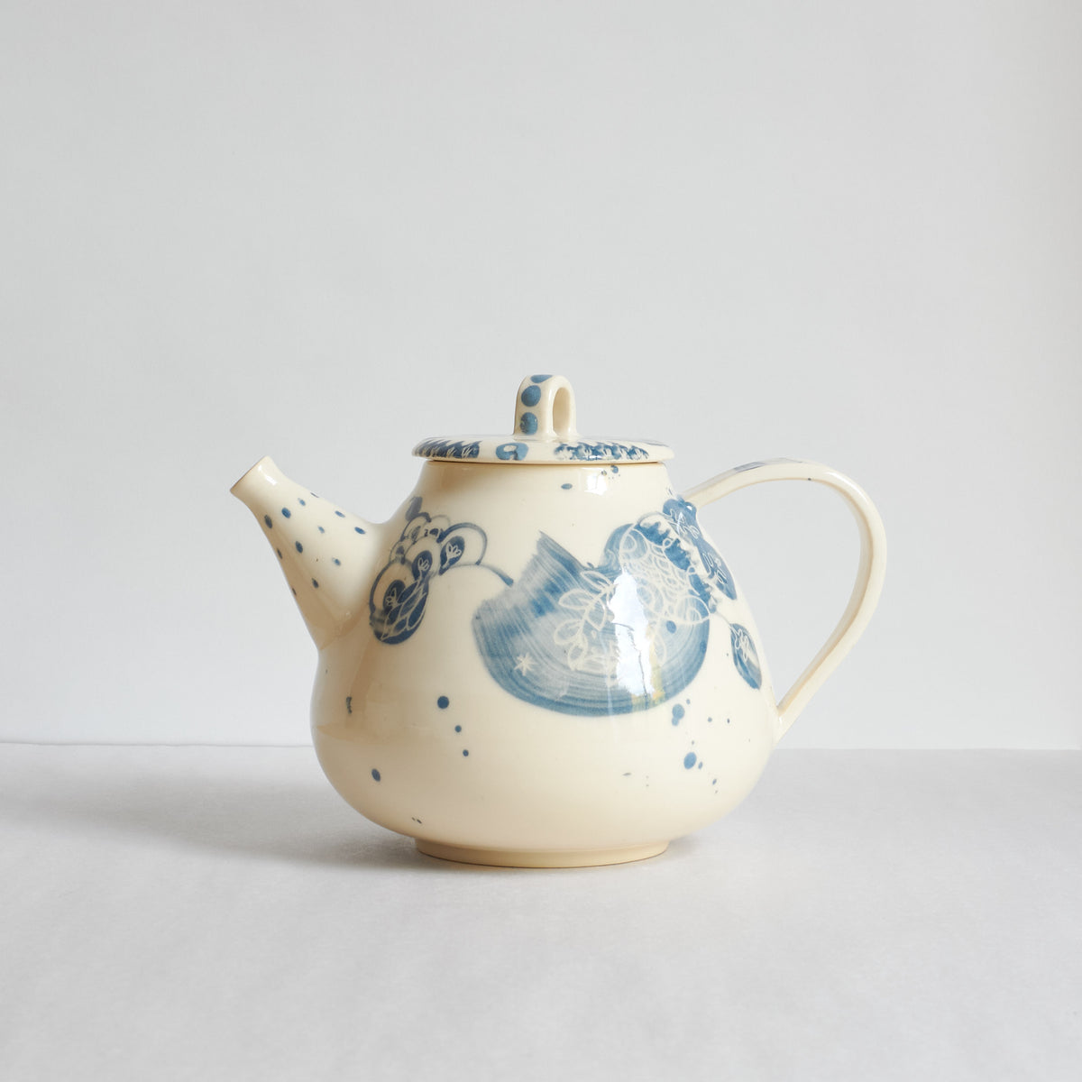 A cream-colored earthenware ceramic teapot with blue hand-painted floral and wave patterns.