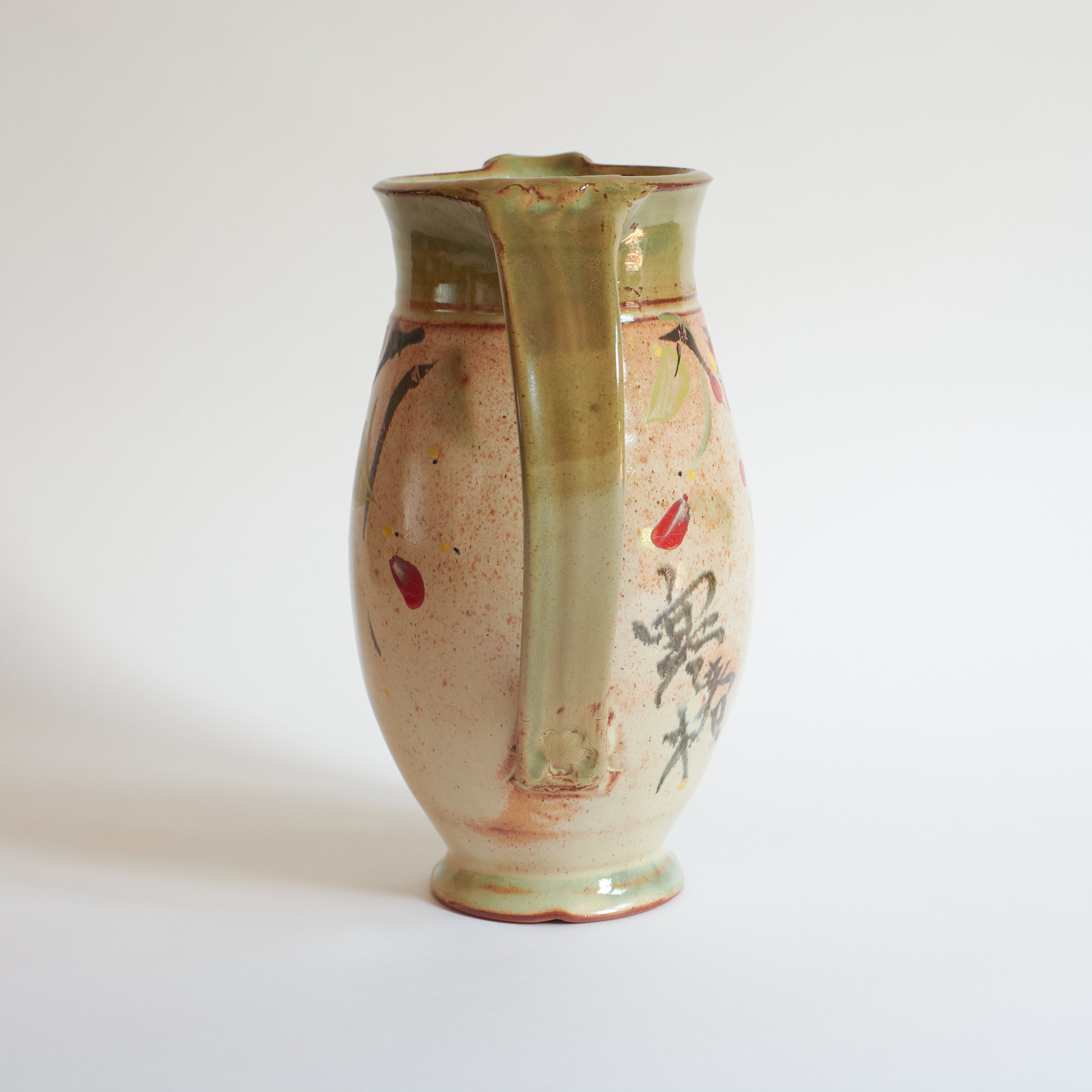 Back of ceramic pitcher with green handle on a white background