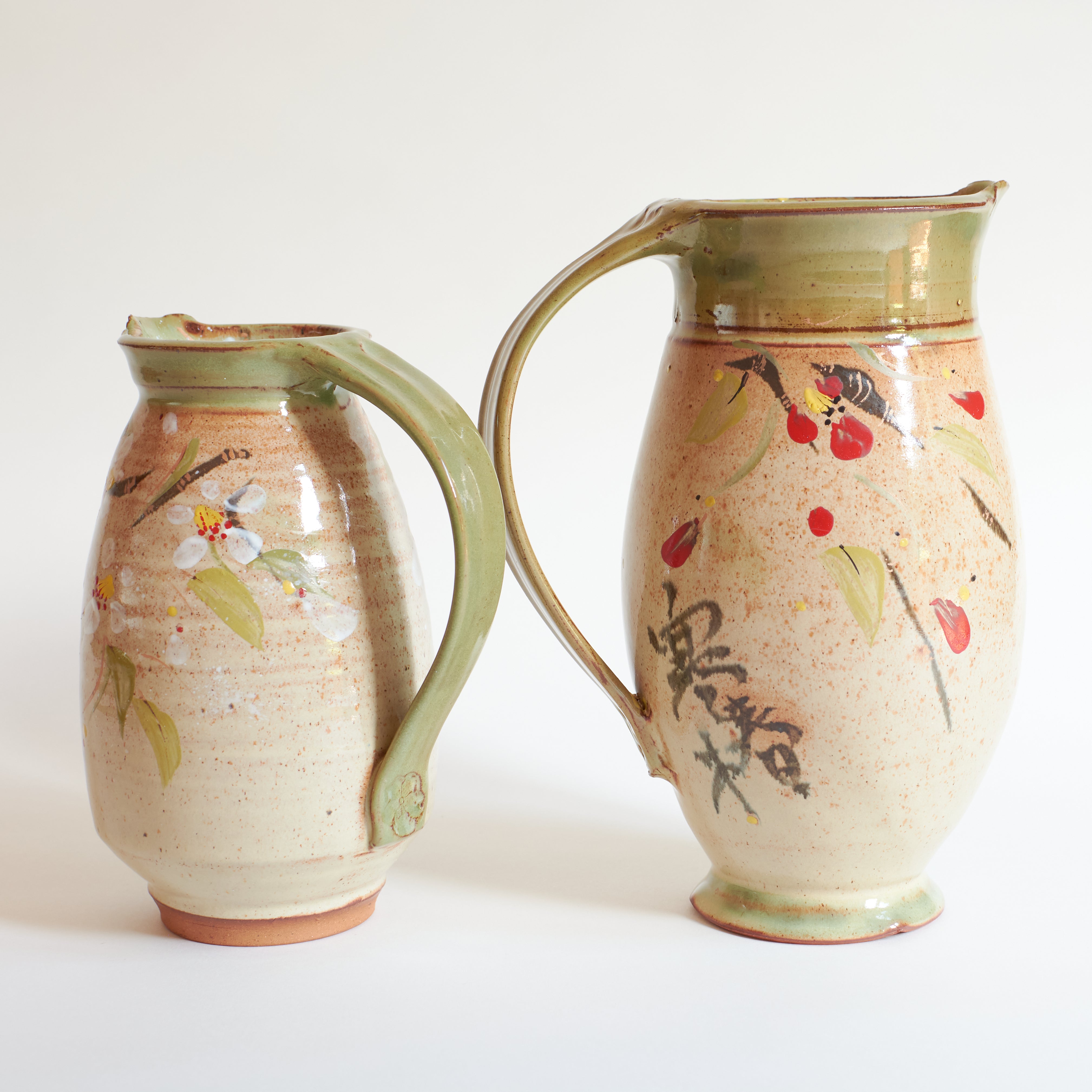 Two ceramic pitchers with floral and leaf designs.