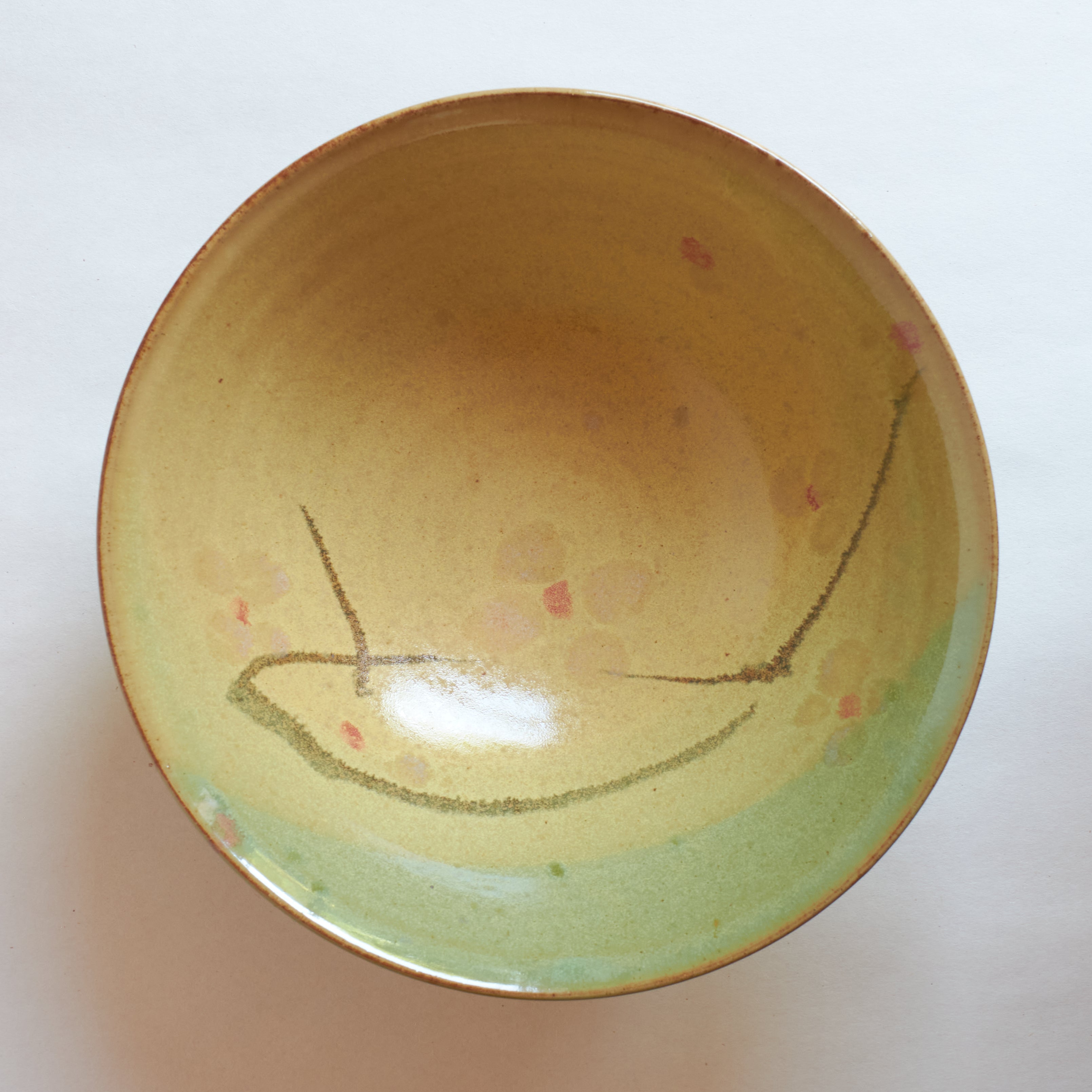 Inside of ceramic bowl with layers of different colored glazes creating a moon and cherry blossoms overlooking green mountains.