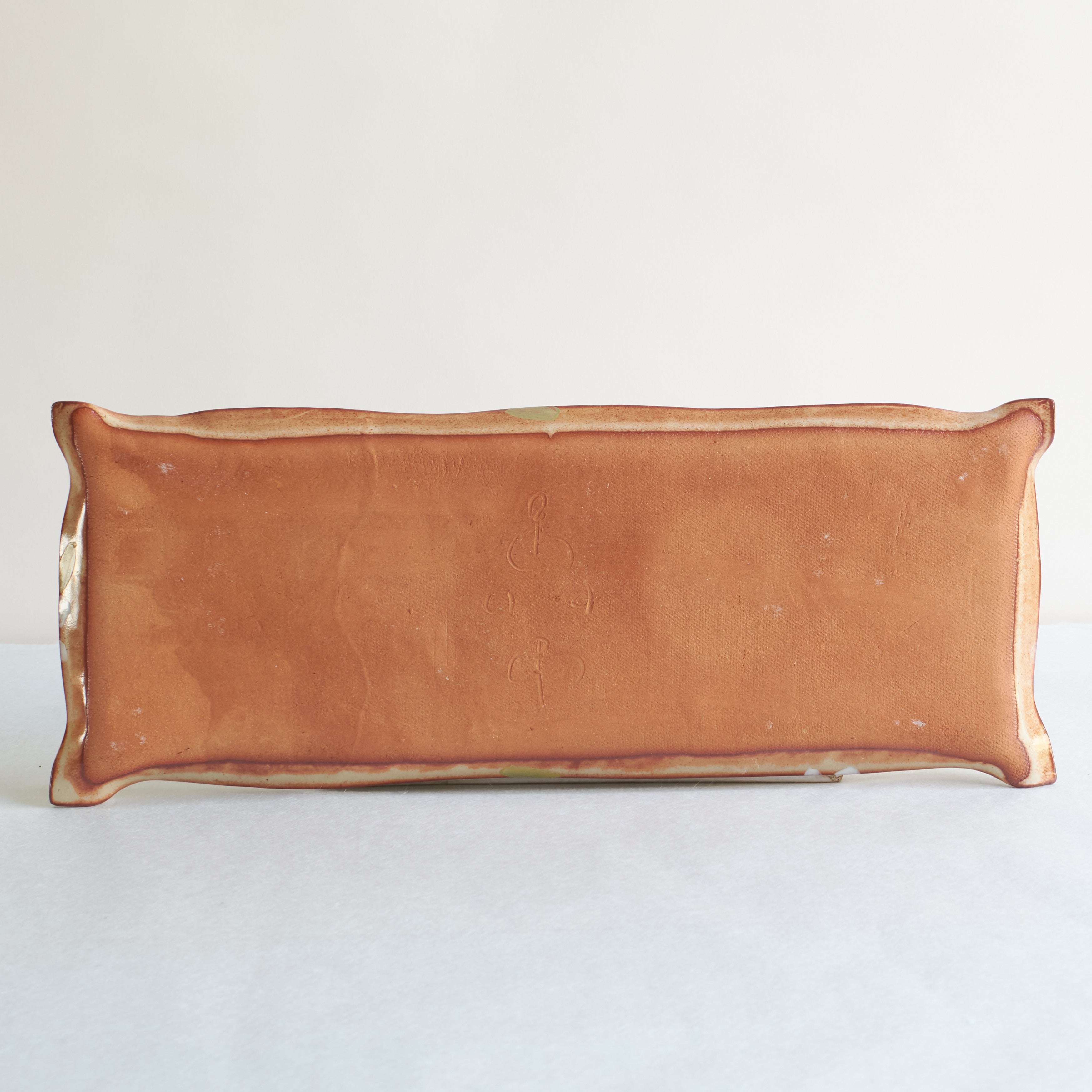 Back of rectangular ceramic dish with red clay on a light gray background