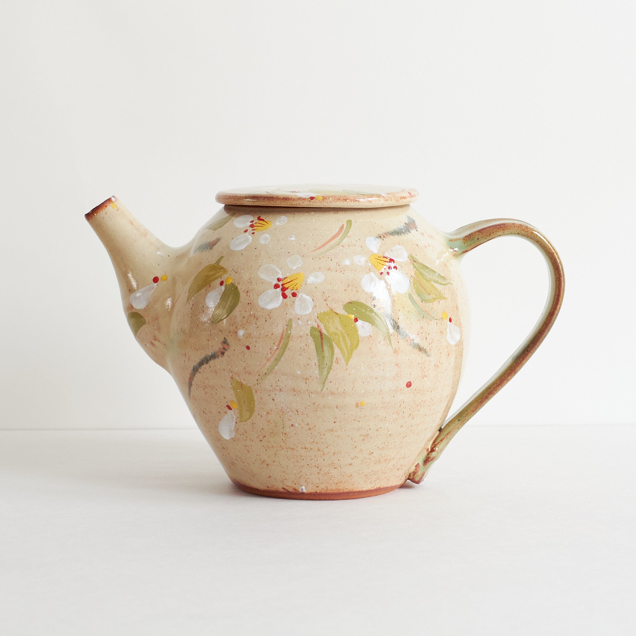 Side view of ceramic teapot with cherry blossom design on a light background