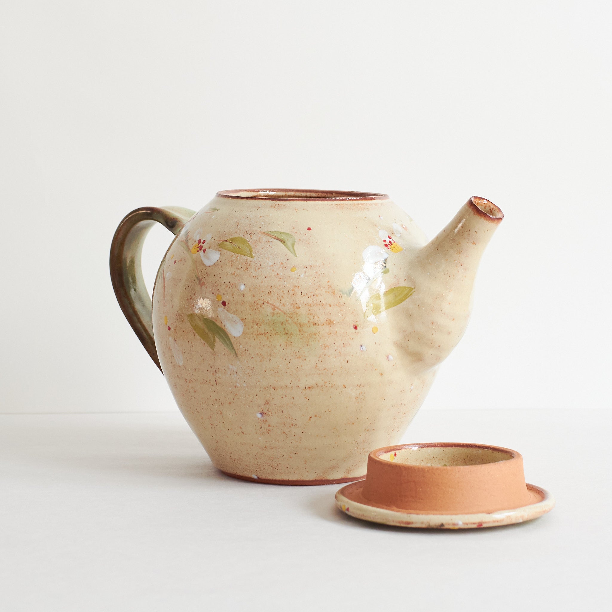 Sideview of ceramic teapot with cherry blossom design on a light background with lid in front