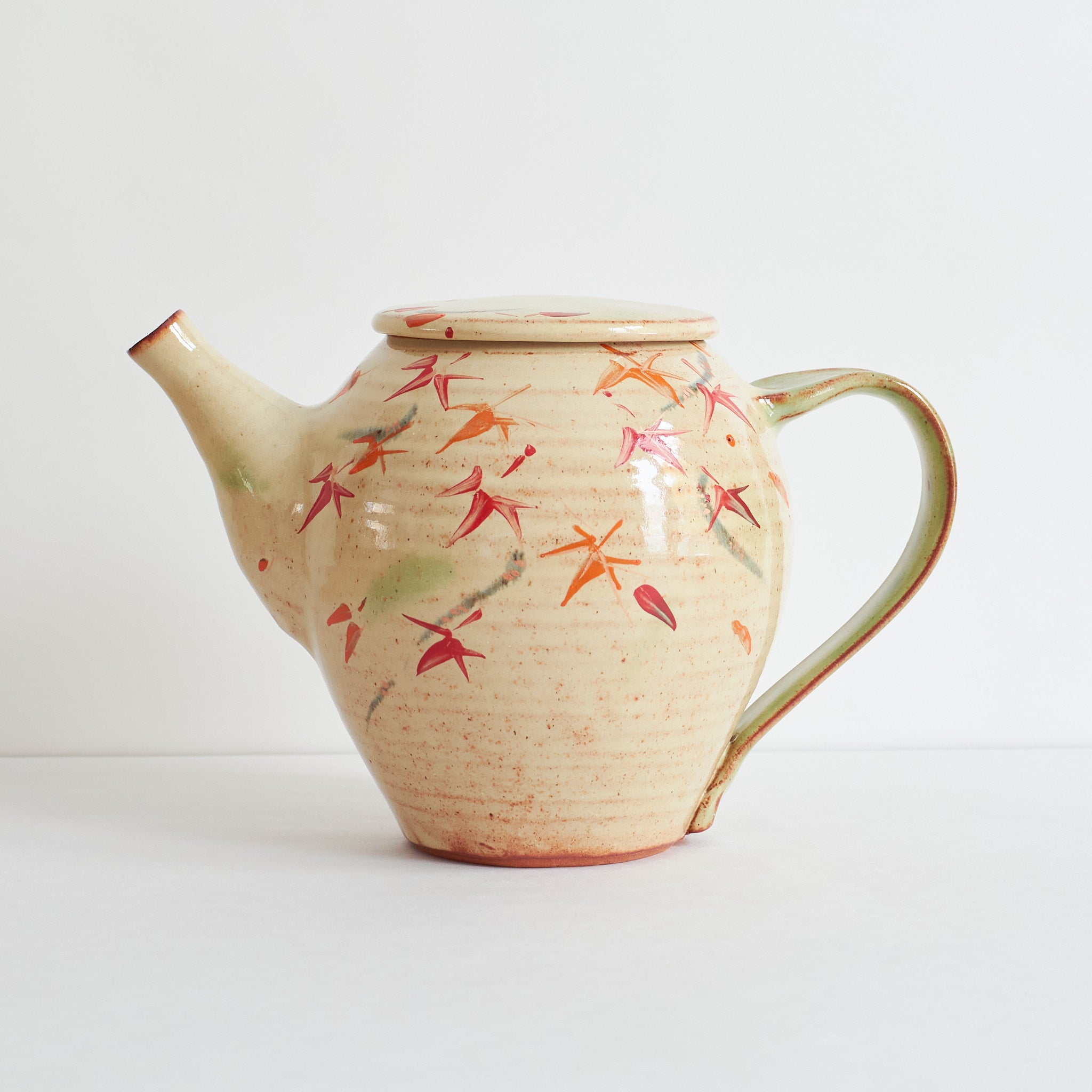 Side view of ceramic teapot with japanese maple tree design on a light background