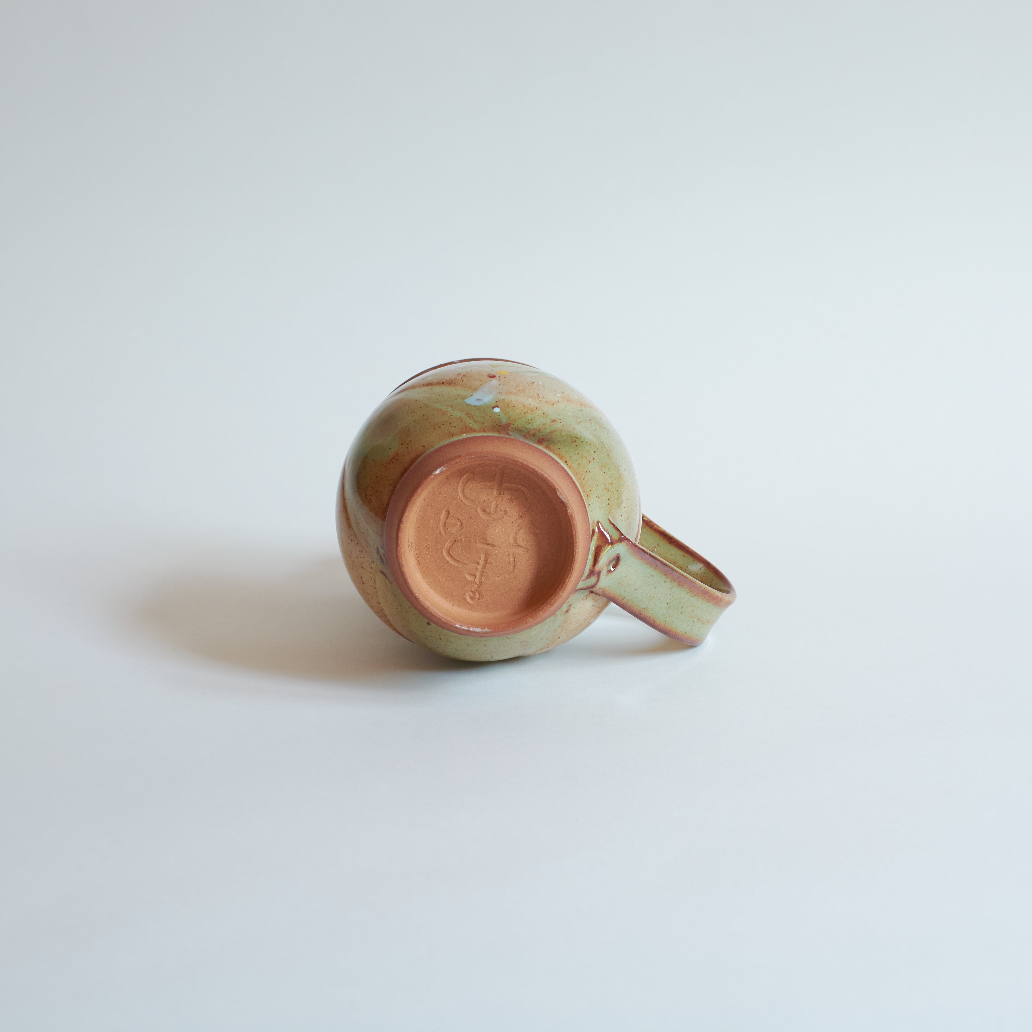 Bottom of red stoneware ceramic mug on a light gray background