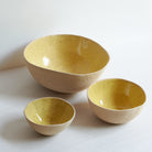Set of small, medium and large yellow bowls made of speckled stoneware 