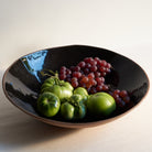 Black bowl with green tomatoes and red grapes on a light background