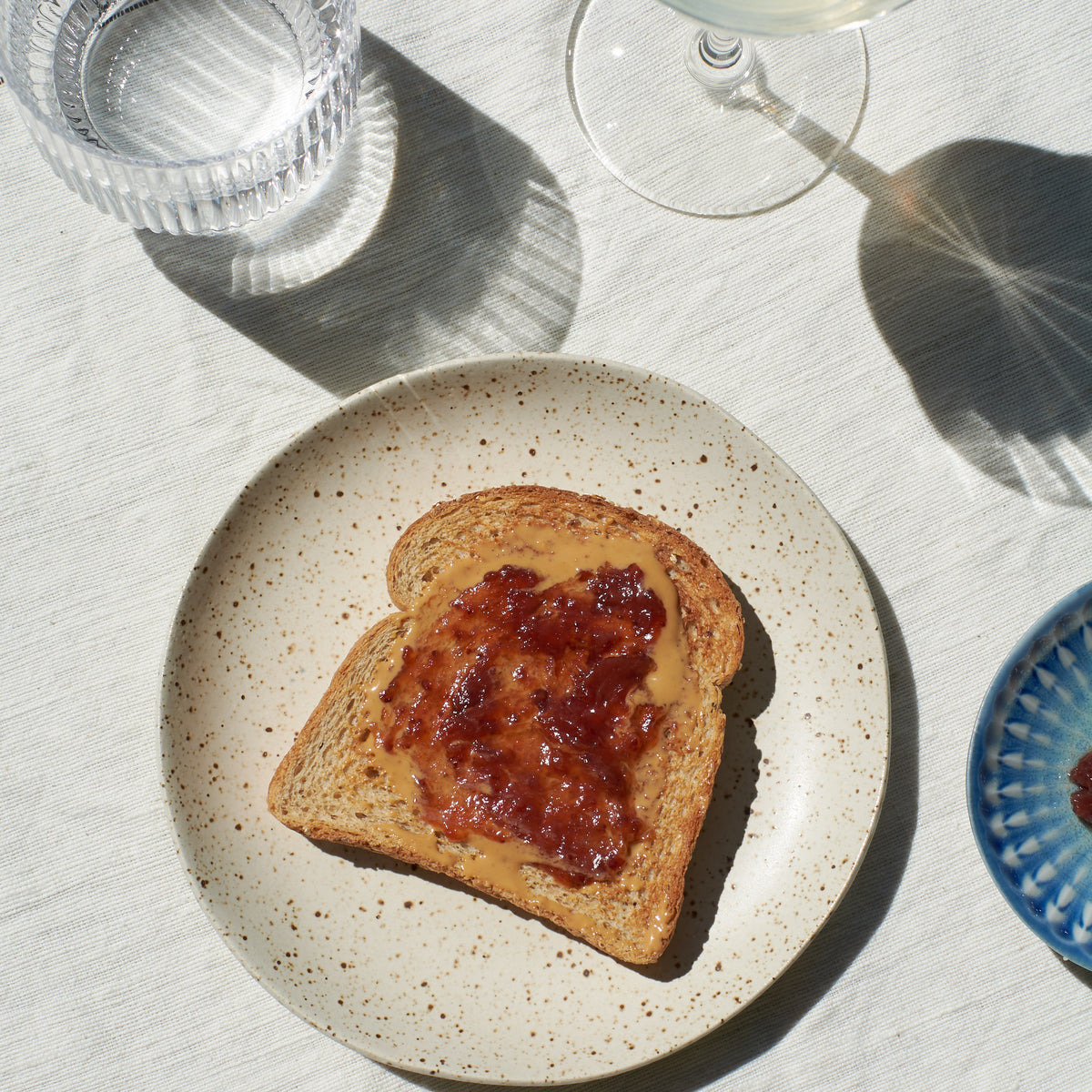 A top-down view of a slice of peanut butter & jam toast on it, served on a speckled beige ceramic plate by Lola Cera.