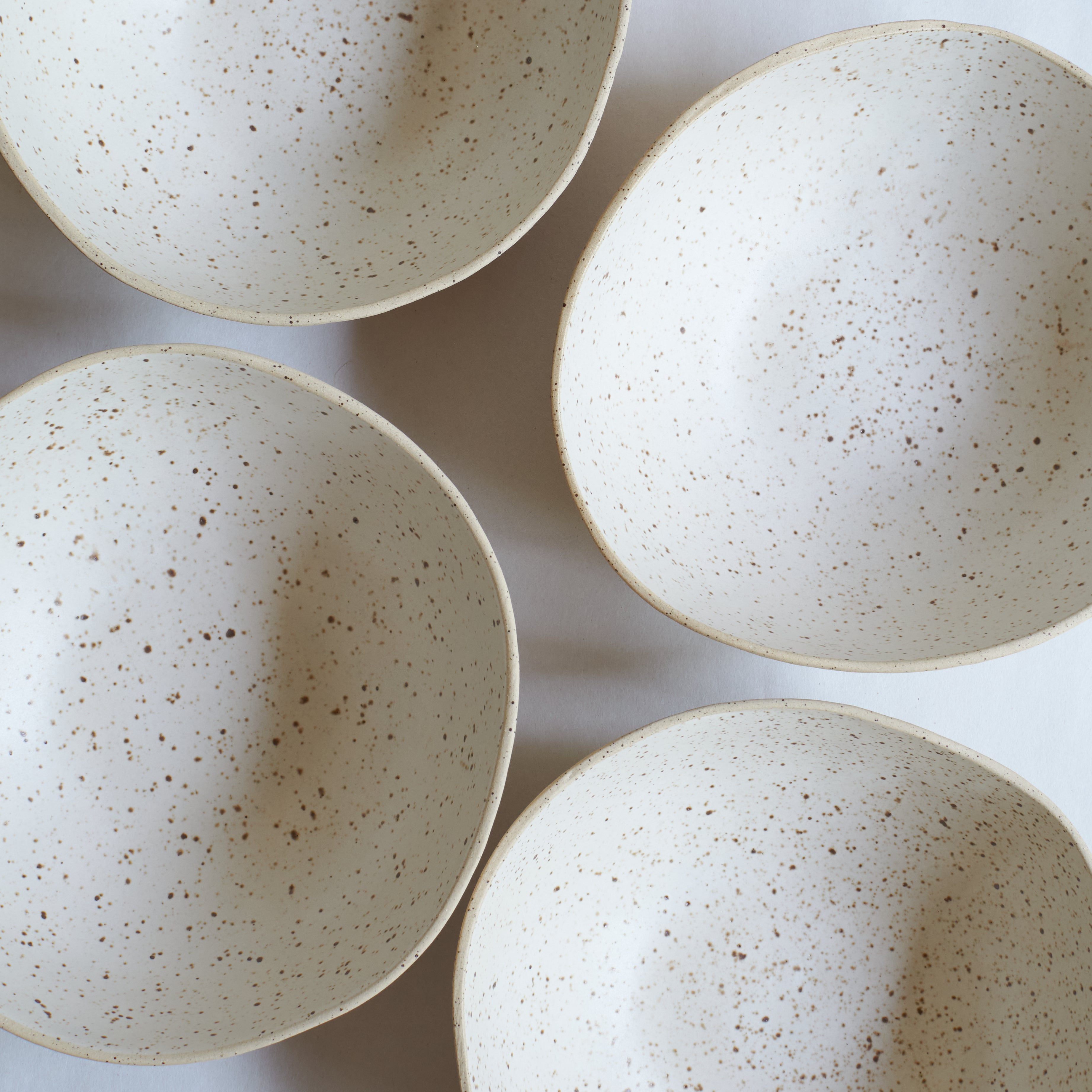 Four large off-white bowls made of speckled stoneware 