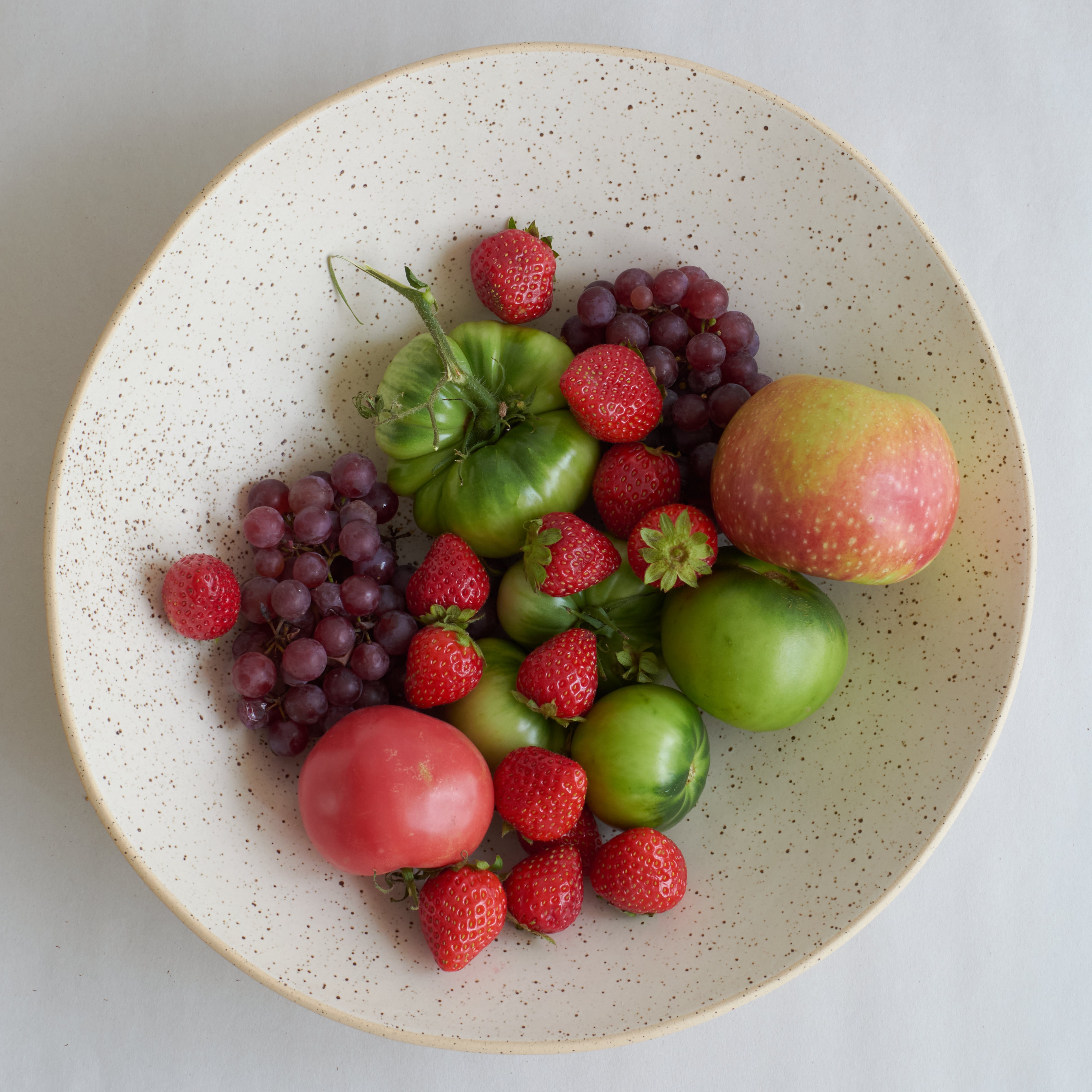 Assorted fruits including grapes, strawberries, and tomatoes on a speckled ceramic plate.