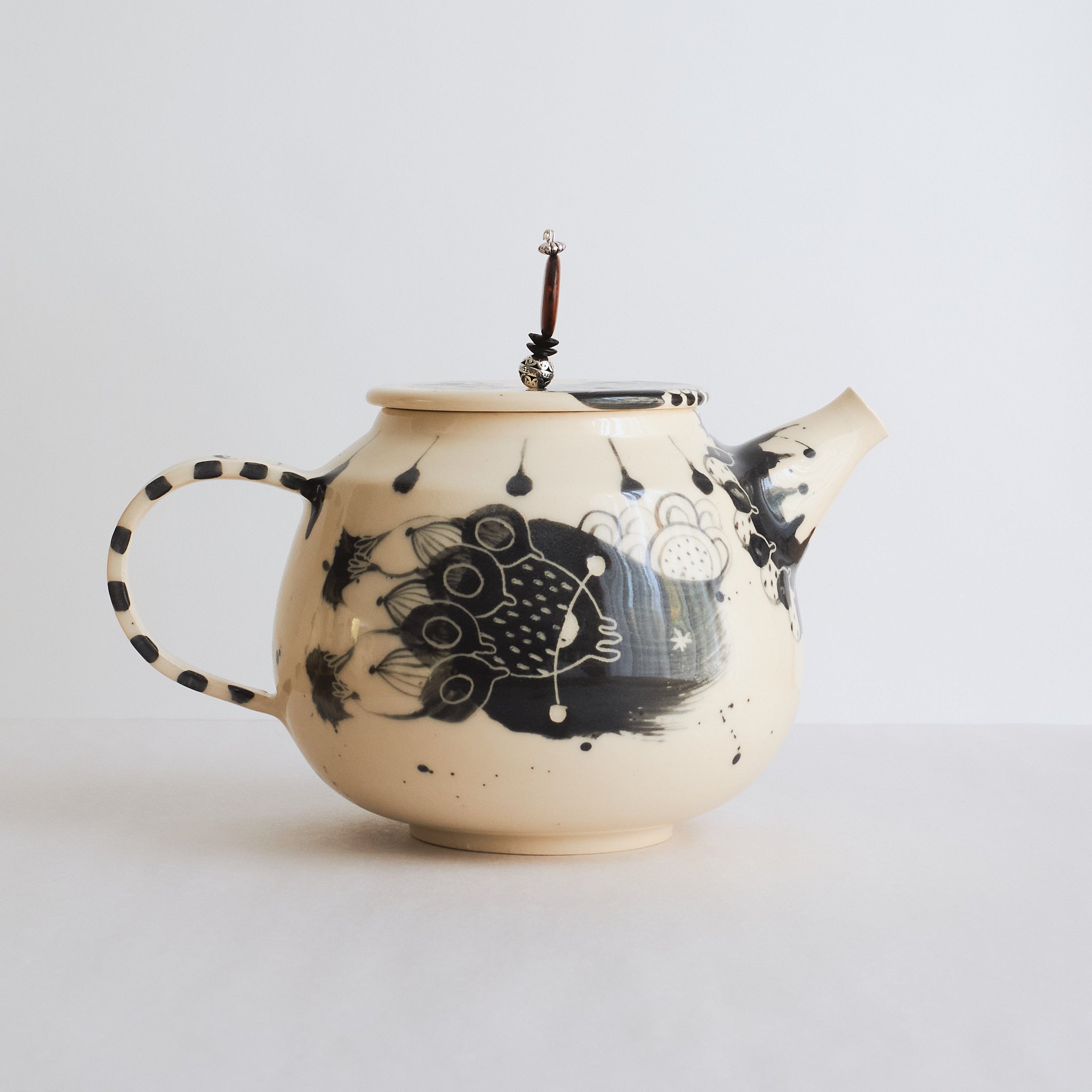 Black and white earthenware teapot with beaded pull on a white background