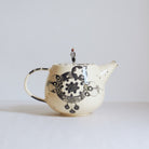 Black and white earthenware teapot with beaded pull on a white background