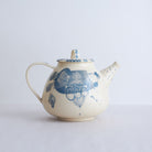 White earthenware teapot with blue carvings on a light gray background