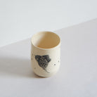 Side view of black and white earthenware tumbler with carved patterns on a light background