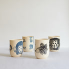 Four earthenware tumblers with carved patterns on a light background