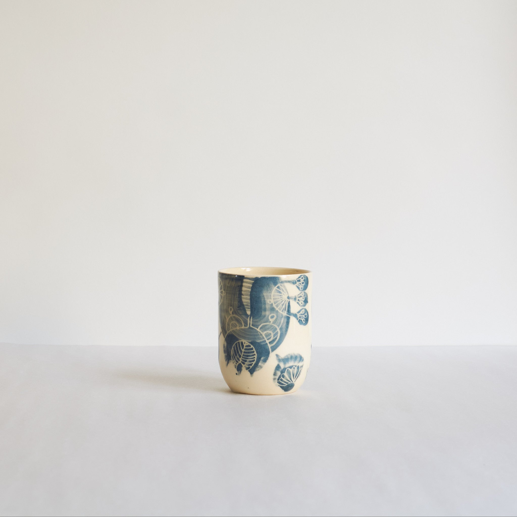 Blue and white earthenware tumbler with carved patterns on a light background
