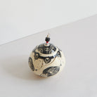 Ceramic lidded box with black carvings on a light gray background