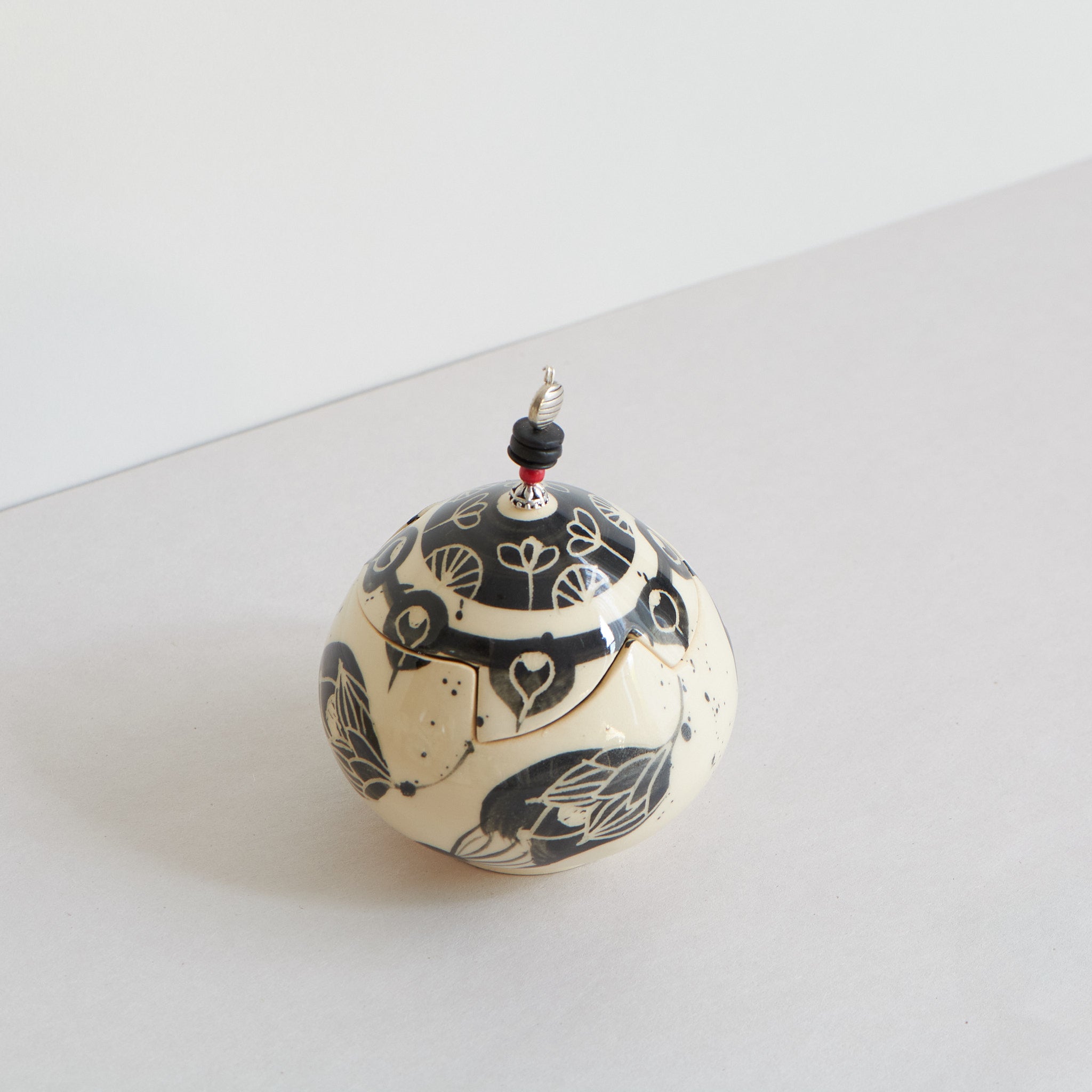 Ceramic lidded box with black carvings on a light gray background