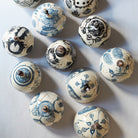 Top view of decorative earthenware lidded boxes with blue carvings and beaded pulls on a light gray background