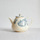 A cream-colored earthenware ceramic teapot with blue hand-painted floral and wave patterns.