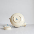 An off-white ceramic teapot with blue hand-painted floral details and a matching lid.