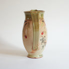 Back of ceramic pitcher with green handle on a white background