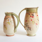 Two ceramic pitchers with floral and leaf designs.