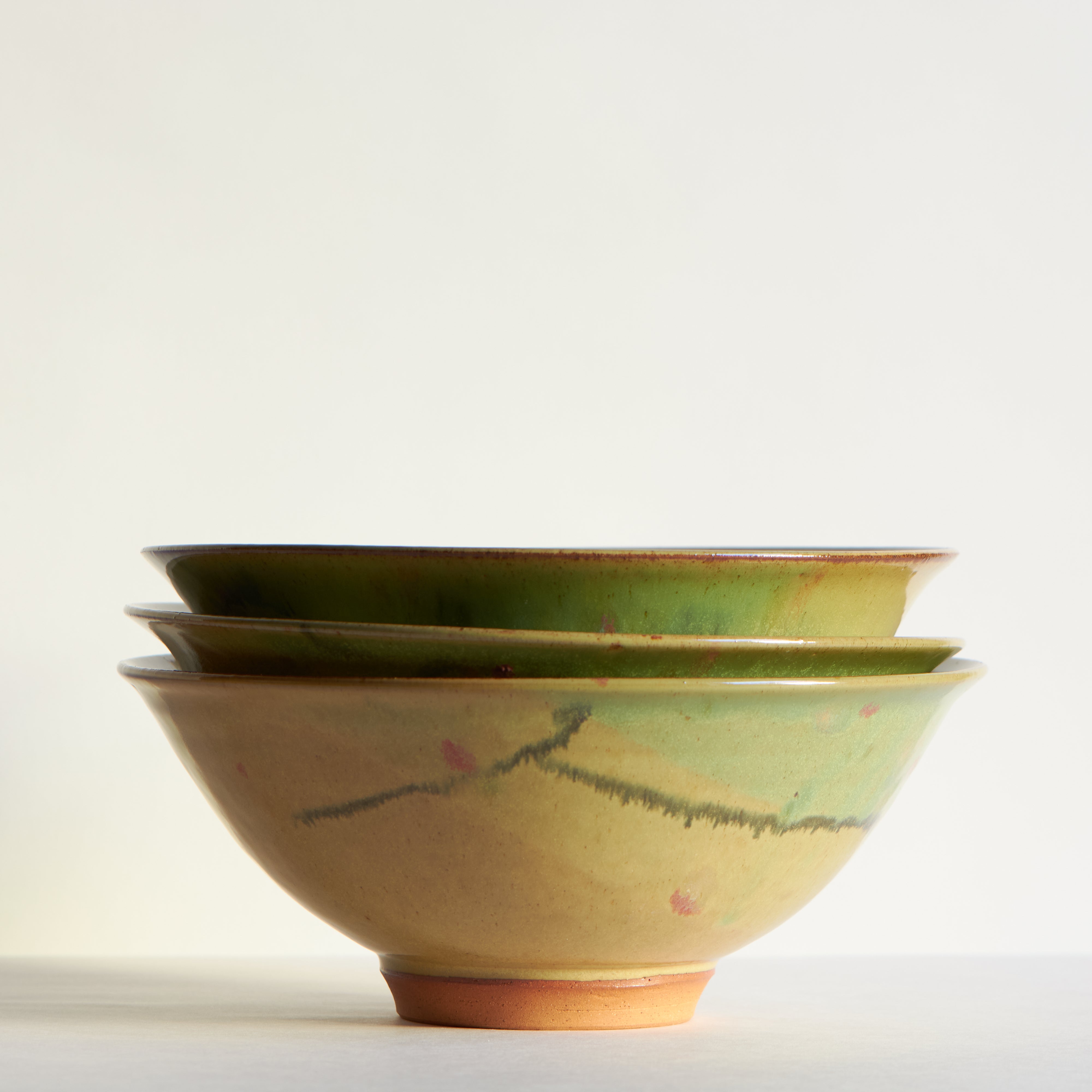 Side view of a set of three ceramic bowls colored with green, shino and dots of red to represent cherry blossoms. 