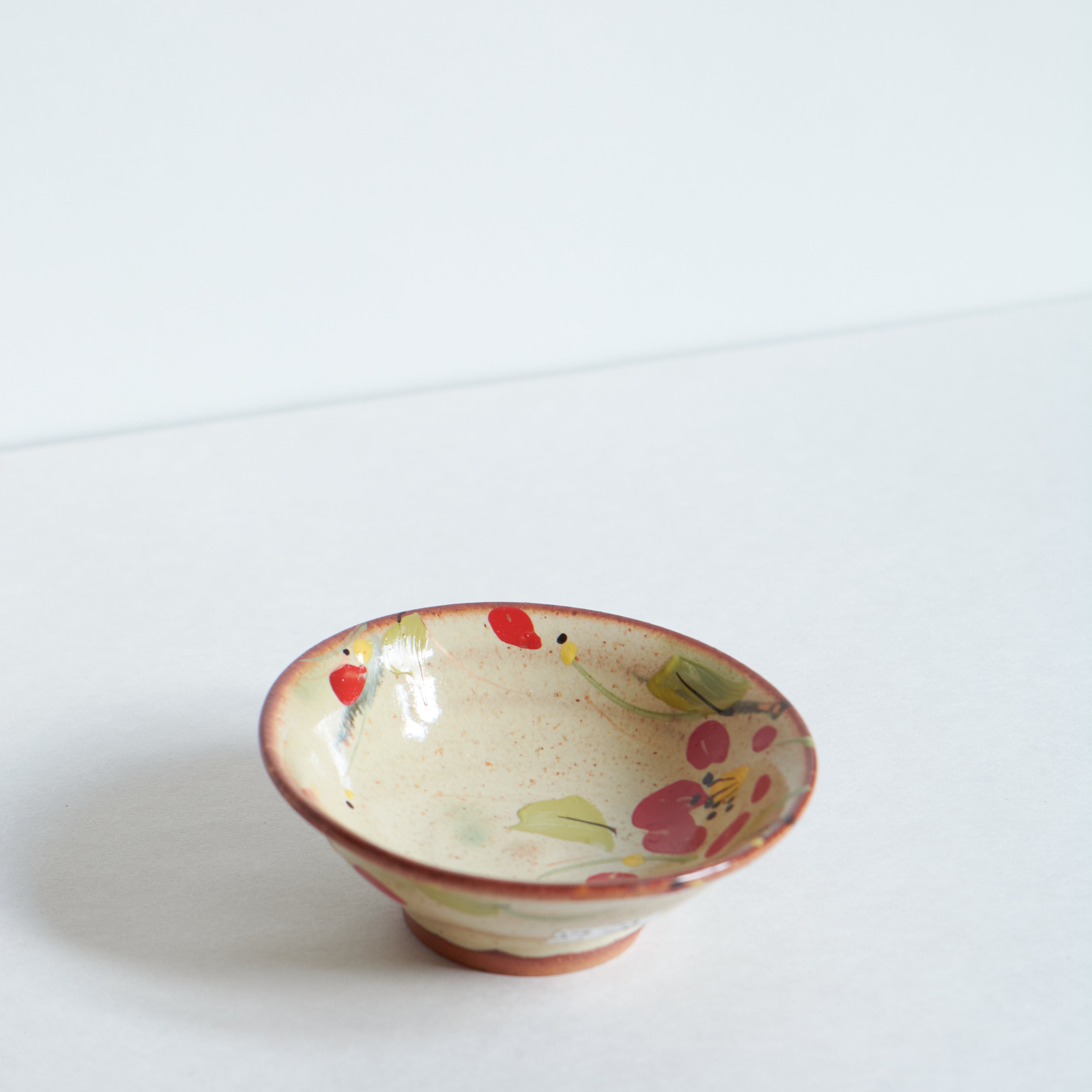Small ceramic bowl with red camellia floral patterns on a white background