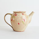 Side view of ceramic teapot with red winter camelia design on a light background