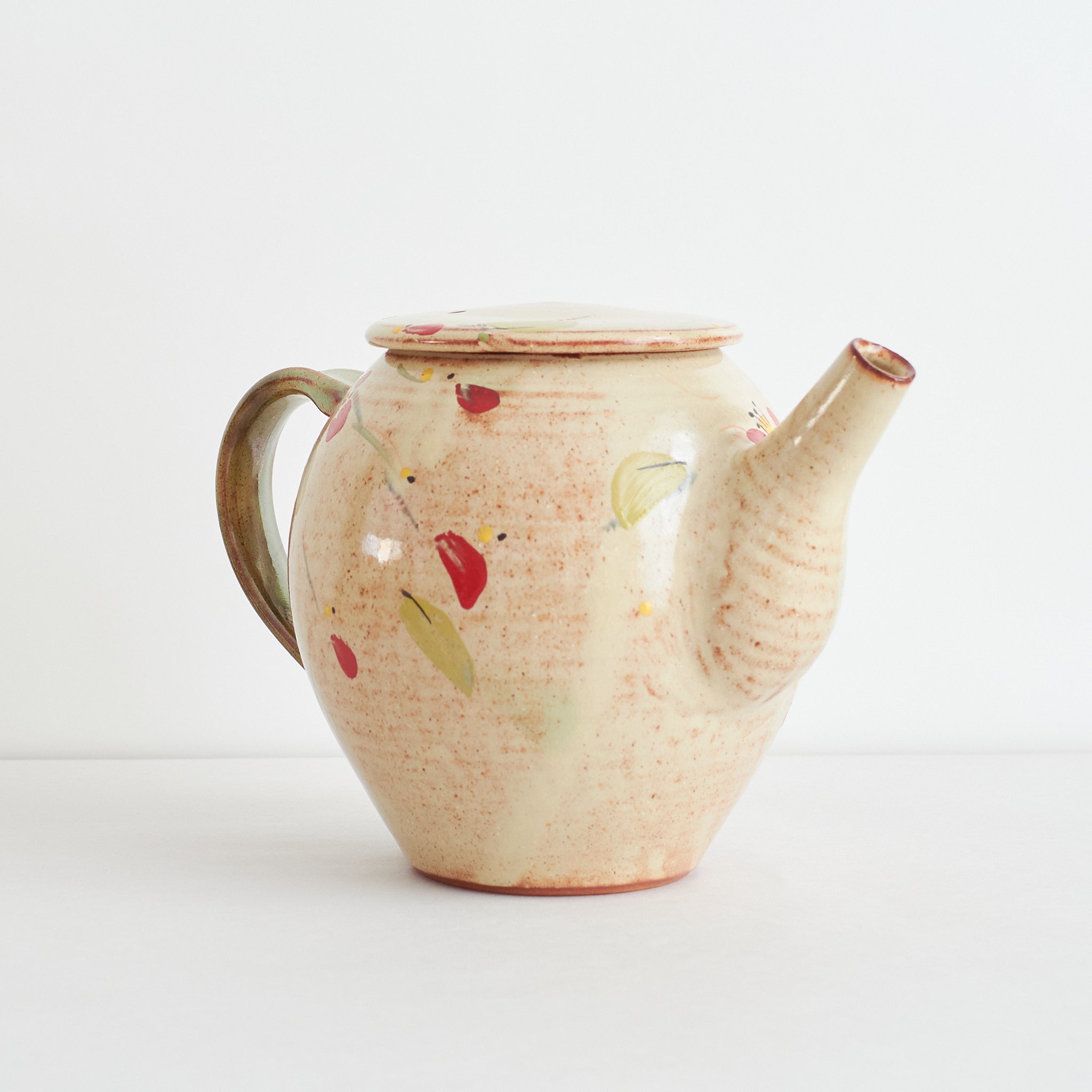 Side view of ceramic teapot with red winter camelia design on a light background