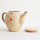 Side view of ceramic teapot with red winter camelia design on a light background with lid off