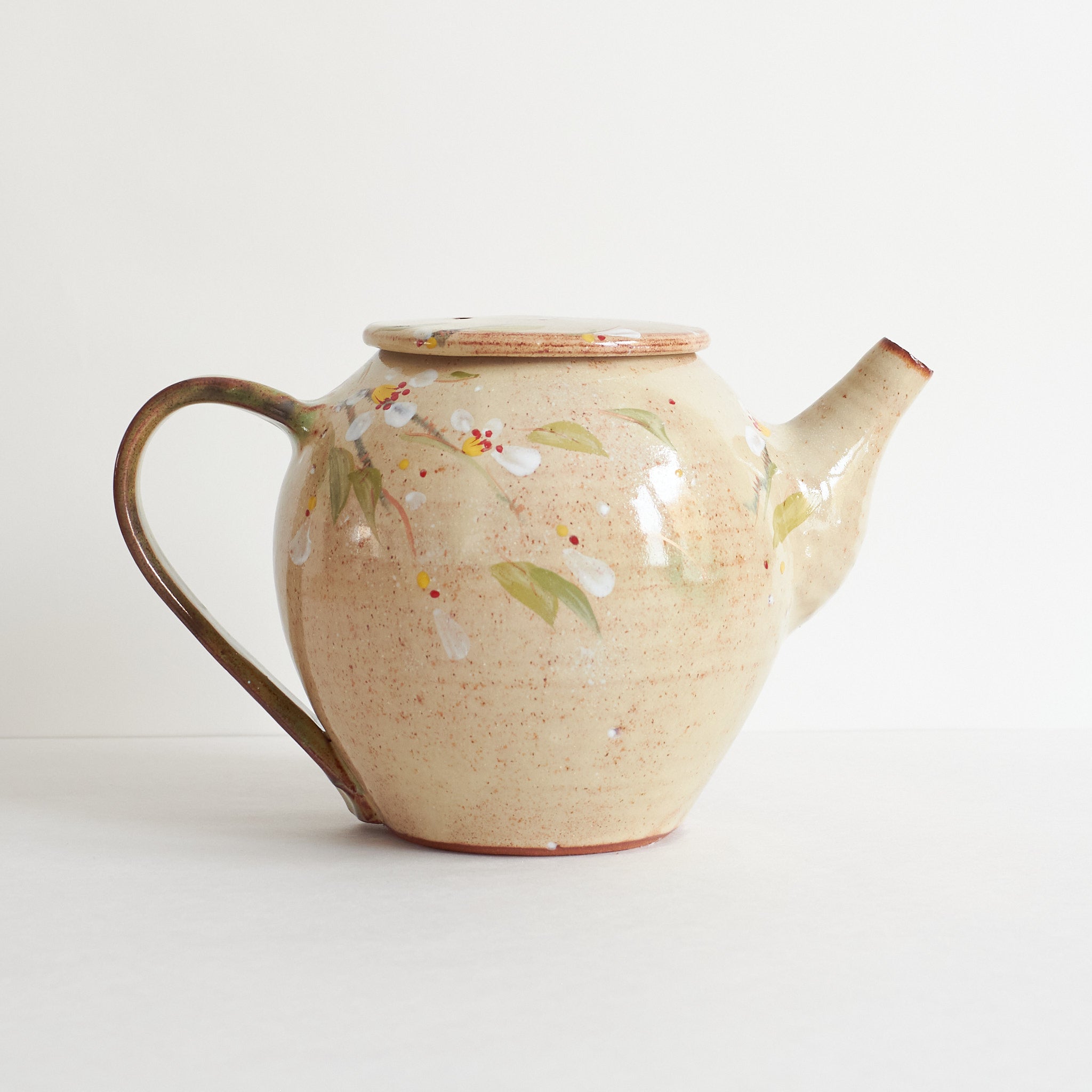 Side view of ceramic teapot with cherry blossom design on a light background