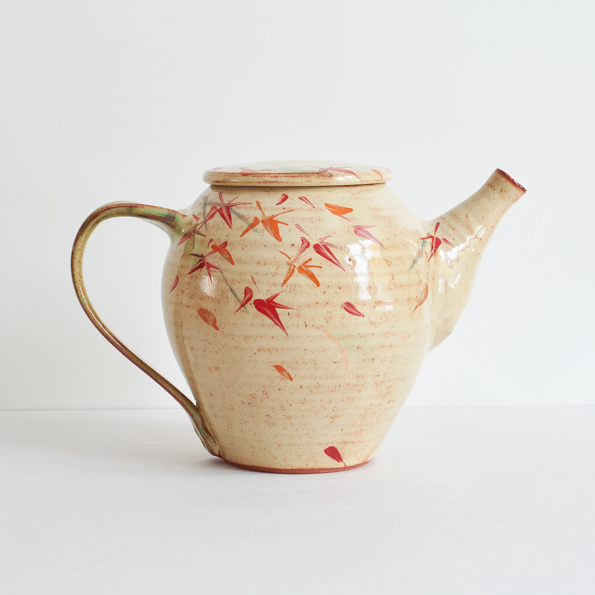 Side view of ceramic teapot with japanese maple tree design on a light background