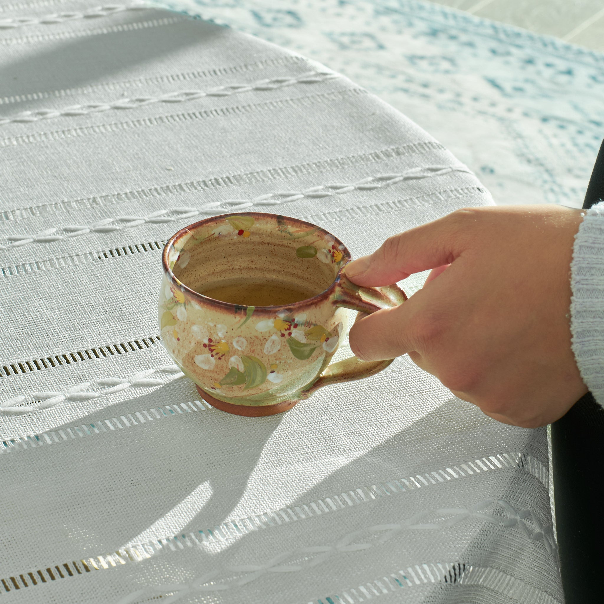 Hand holding a Yukari Hazama spring cherry cappuccino cup on a white tablecloth.