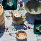 Ceramic teapot and bowls on a textured tablecloth with red peppers.