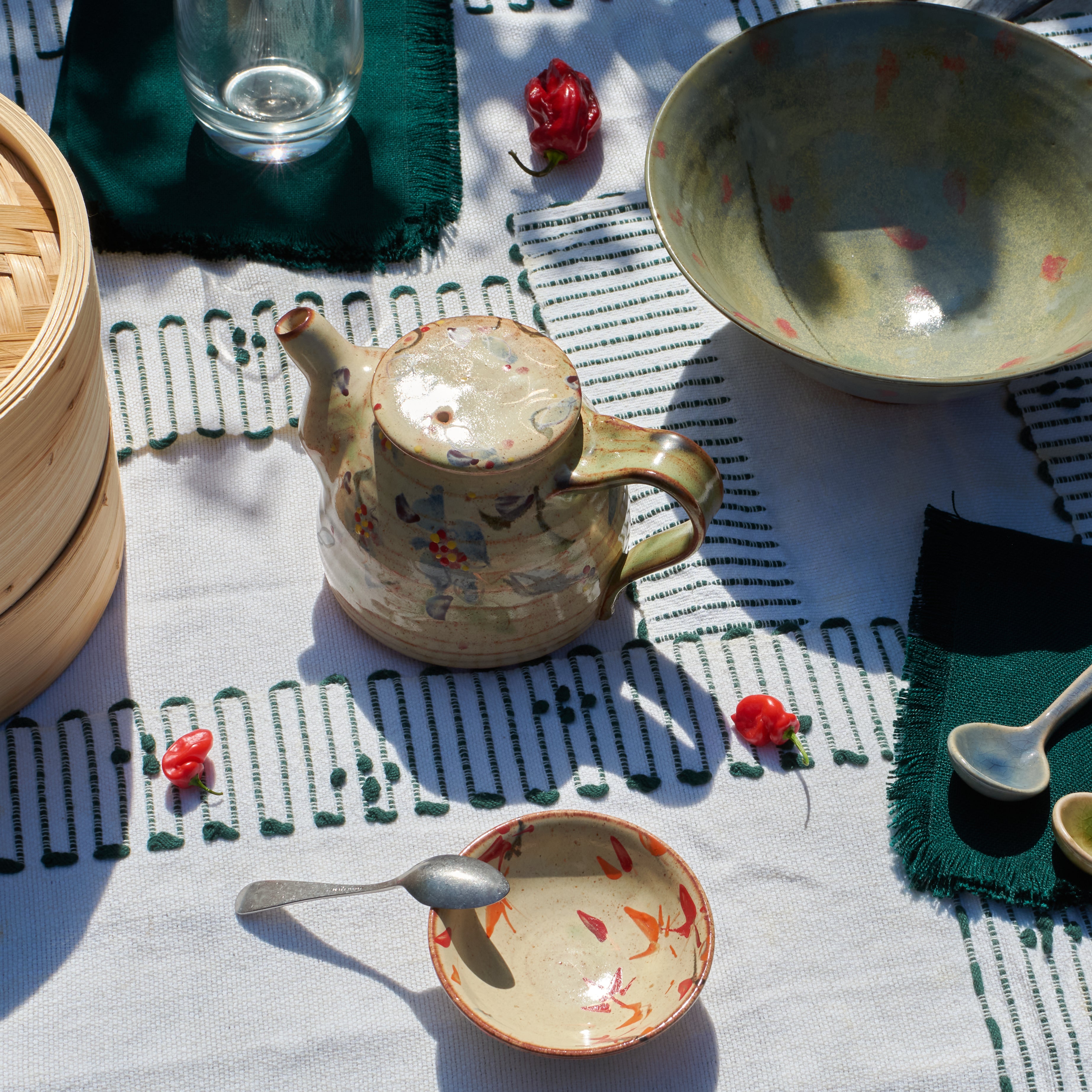 Ceramic teapot and bowls on a textured tablecloth with red peppers.